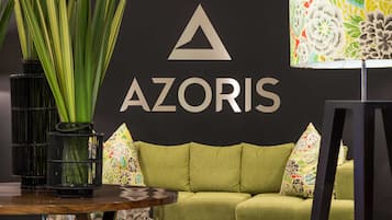 Een kamer met een groene bank, een zwarte muur met het AZORIS logo, en een kleurrijke bloemenlamp.