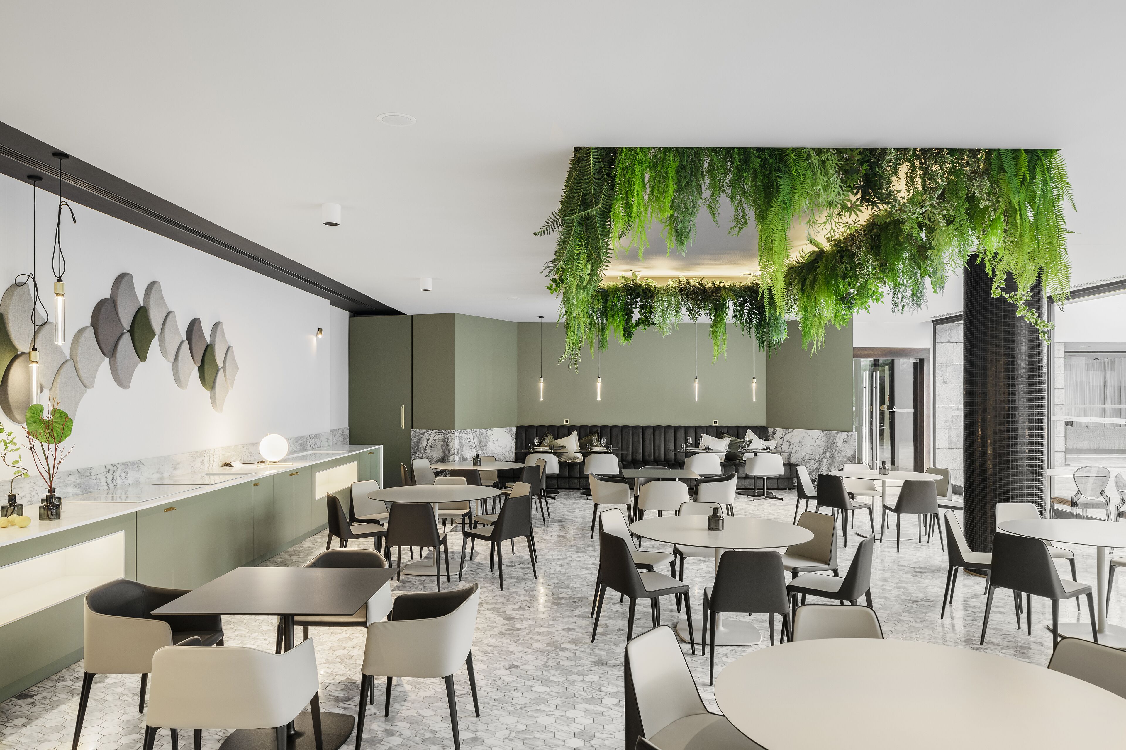 Un restaurante moderno con una instalación de plantas colgantes verdes, suelo de mármol y mobiliario contemporáneo.
