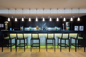 A bar area with a long counter, multiple hanging pendant lights, and several bar stools with patterned cushions.