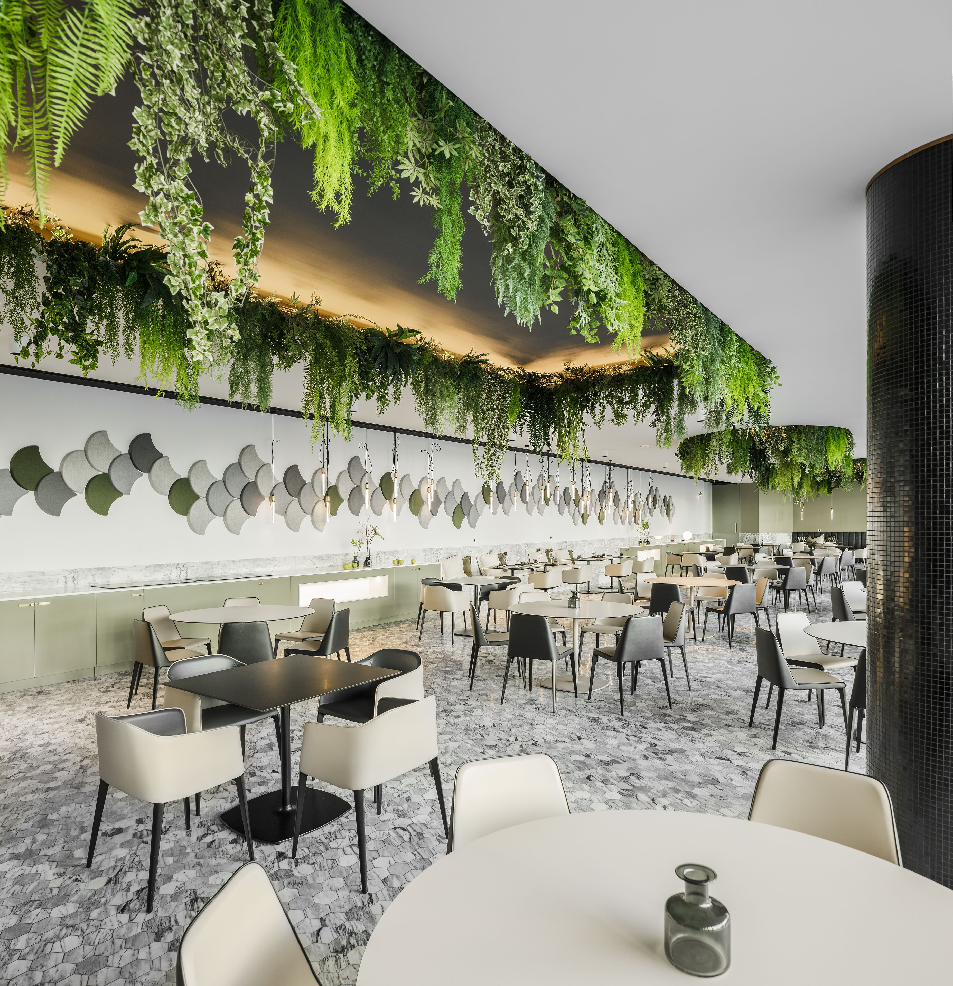 A modern dining area with round tables and chairs, a decorative wall with hanging plants, and a patterned floor.