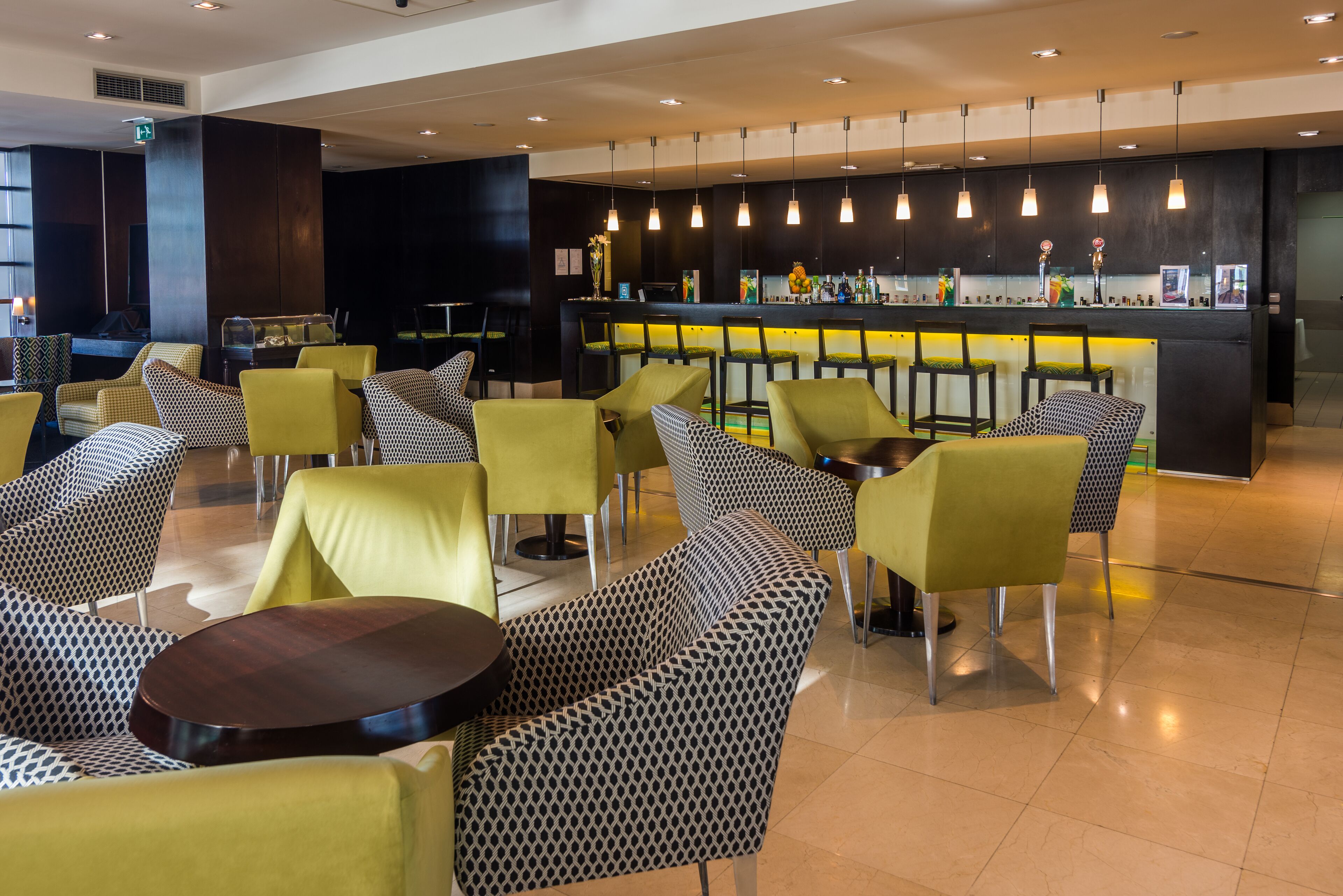 Een moderne bar met een toog, diverse zitmogelijkheden inclusief gestreepte stoelen en tafels, en hangende verlichting.
