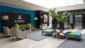 Un vestíbulo moderno con techo alto, zona de estar central con sofás y sillones, una mesa de centro y una planta grande en maceta.