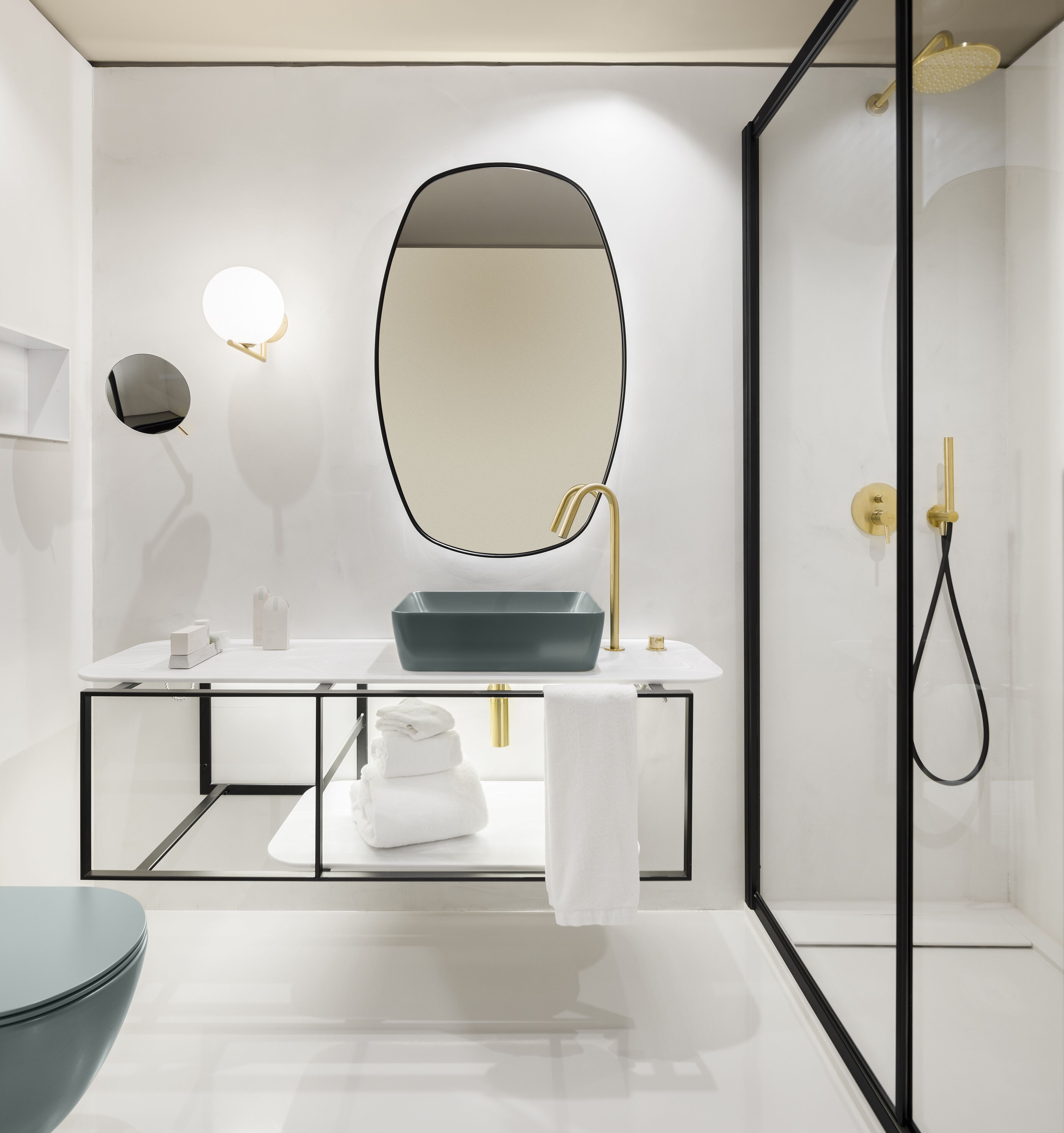 A modern bathroom with a large oval mirror, a rectangular sink with a gold faucet, and a glass-enclosed shower.