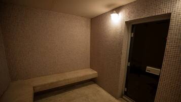 A small, tiled bathroom with a bench, a door, and a light fixture.