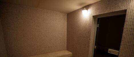 Un baño pequeño con azulejos, una banca, una puerta y una lámpara.