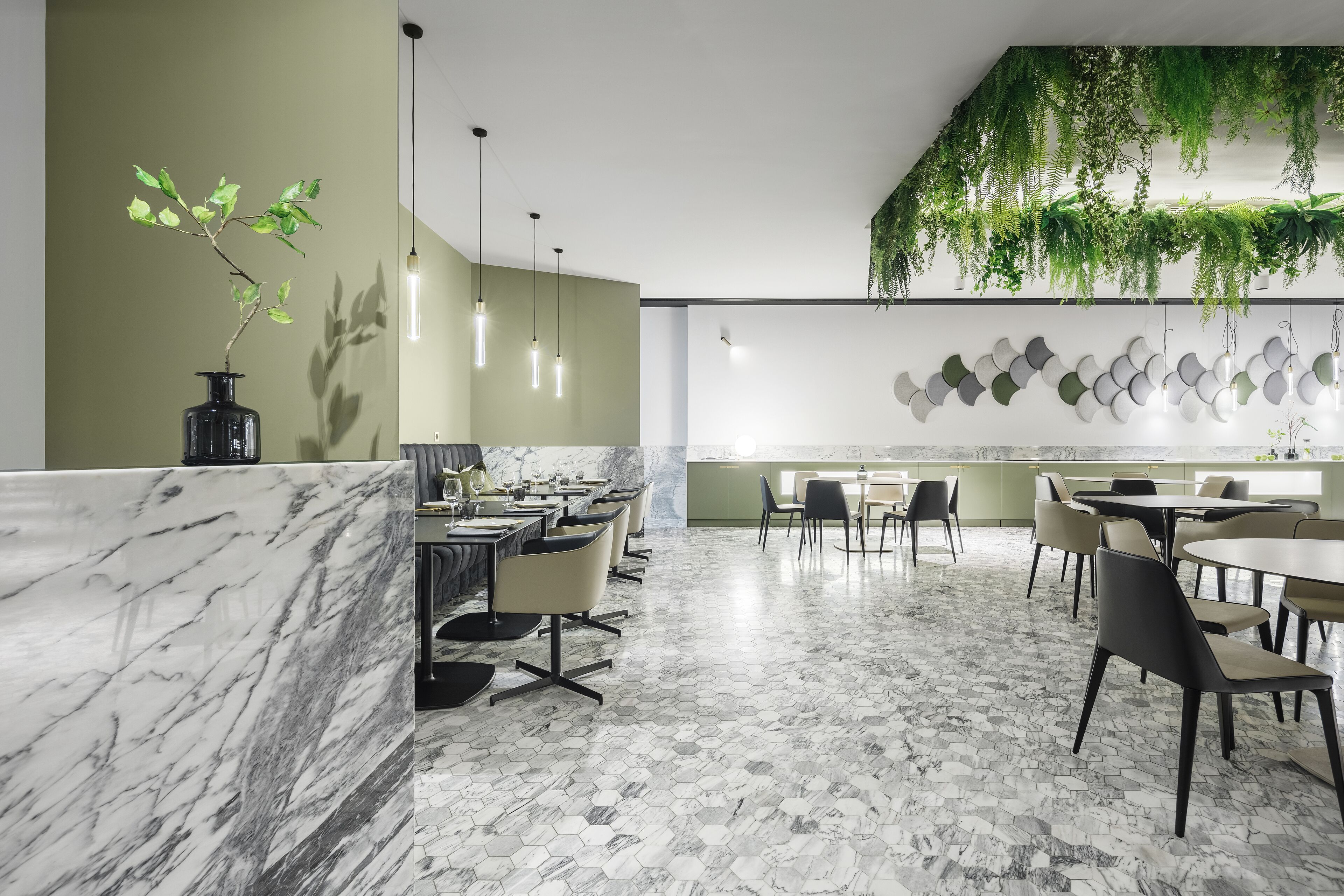Un restaurant moderne doté d’un bar en marbre, d’un sol à motifs hexagonaux, de plantes suspendues, de luminaires suspendus et d’un mur orné de miroirs ronds.