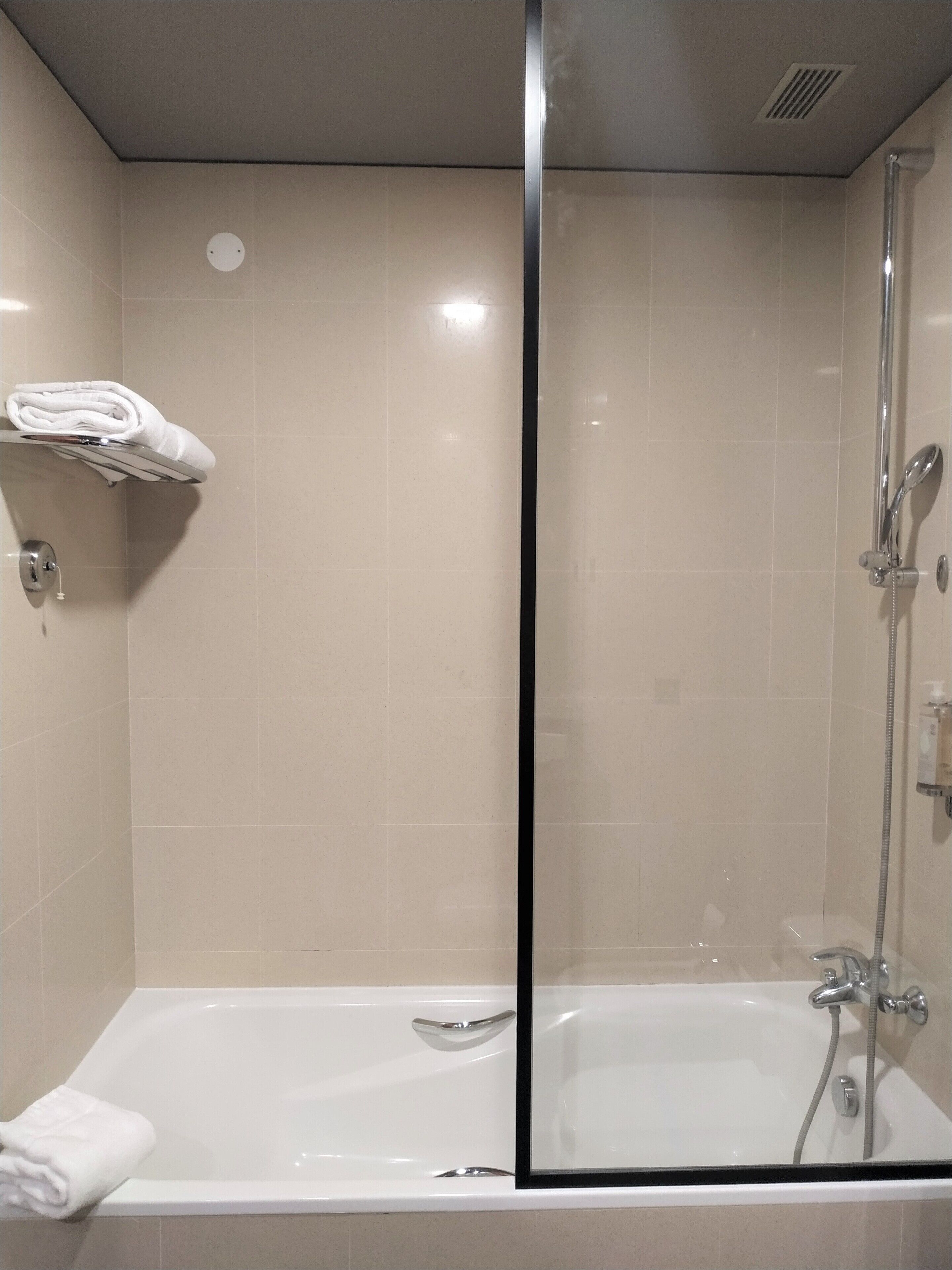A modern bathroom with a glass-enclosed shower, a white bathtub, and a towel rack with folded towels.