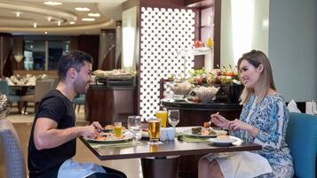 Een koppel dineert aan een tafel in een modern restaurant van een hotel, met een buffet op de achtergrond.