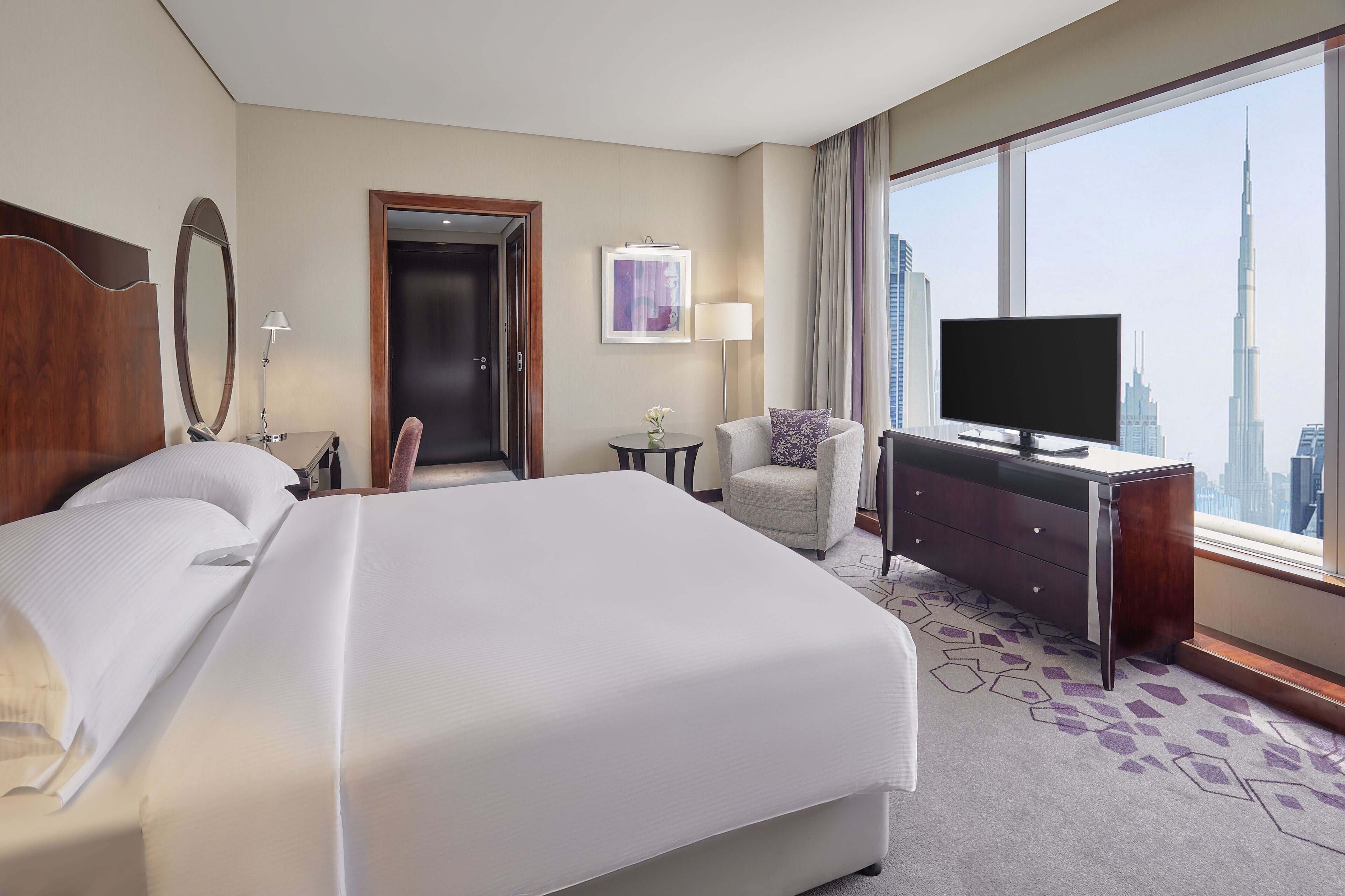 Une chambre d’hôtel avec un grand lit, une télévision, un bureau et une vue sur le panorama urbain.