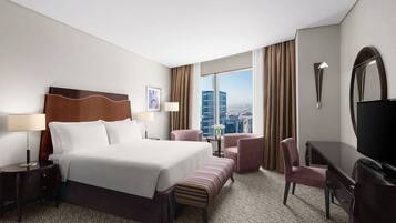 Een hotelkamer met een groot bed, een bureau, een stoel, een televisie en uitzicht op de stad.