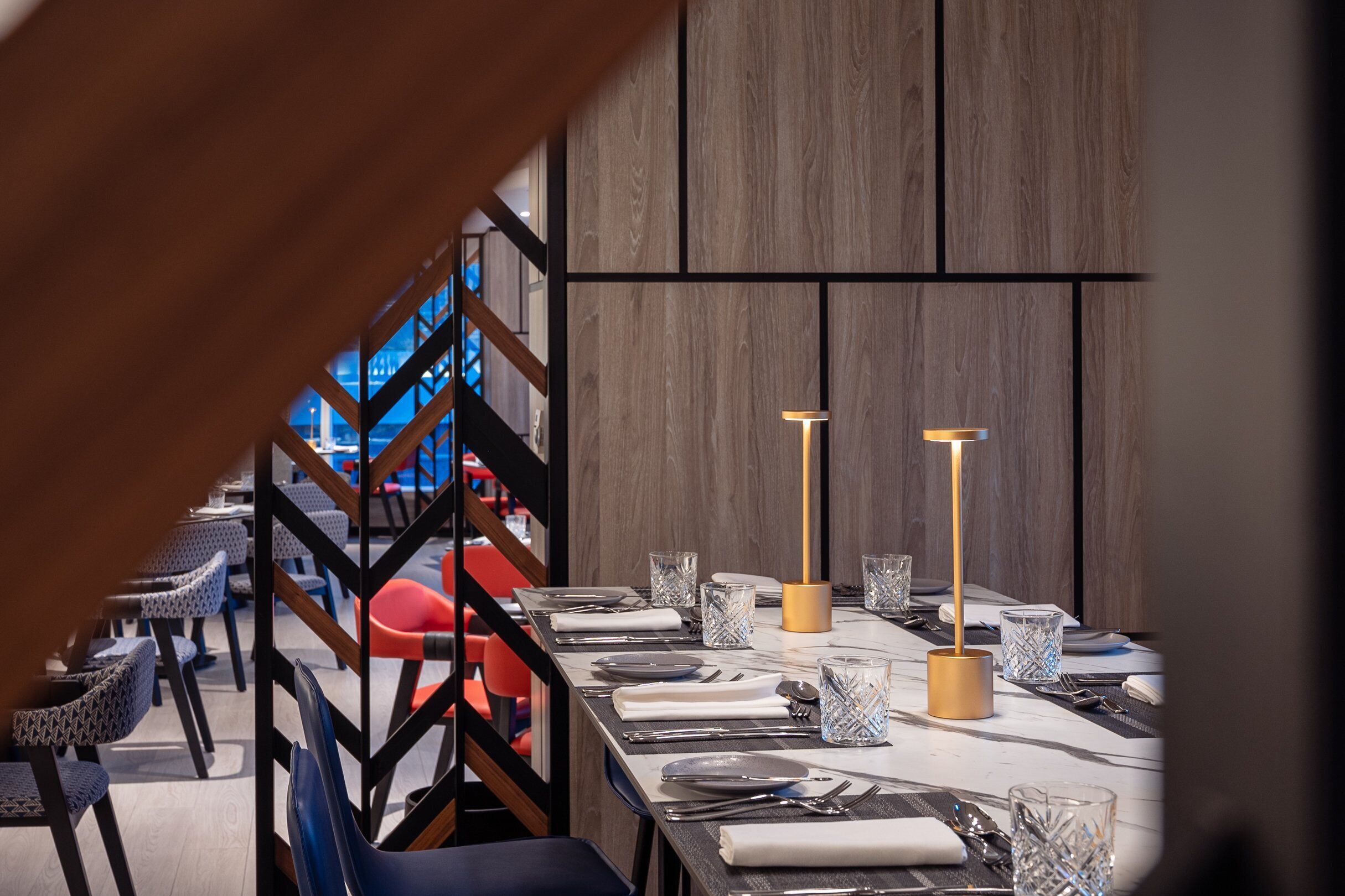Un espace de restauration moderne avec une longue table dressée pour un repas, agrémenté de verres et de couverts.