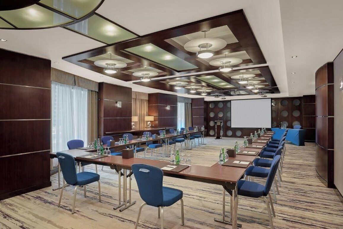 A conference room with a long table, blue chairs, and a projector screen.
