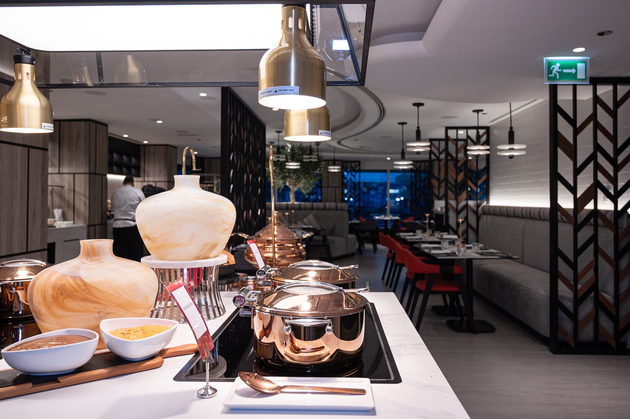 Interior moderno de restaurante con una barra de buffet, que incluye diversos platos y equipo de cocina.