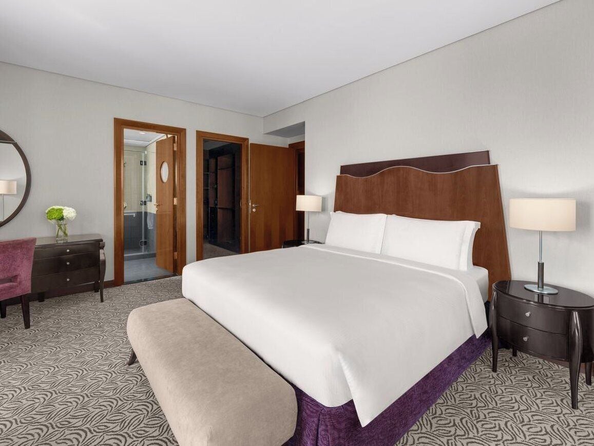 Een hotelkamer met een groot bed, nachtkastjes, een bankje, een dressoir en een spiegel.