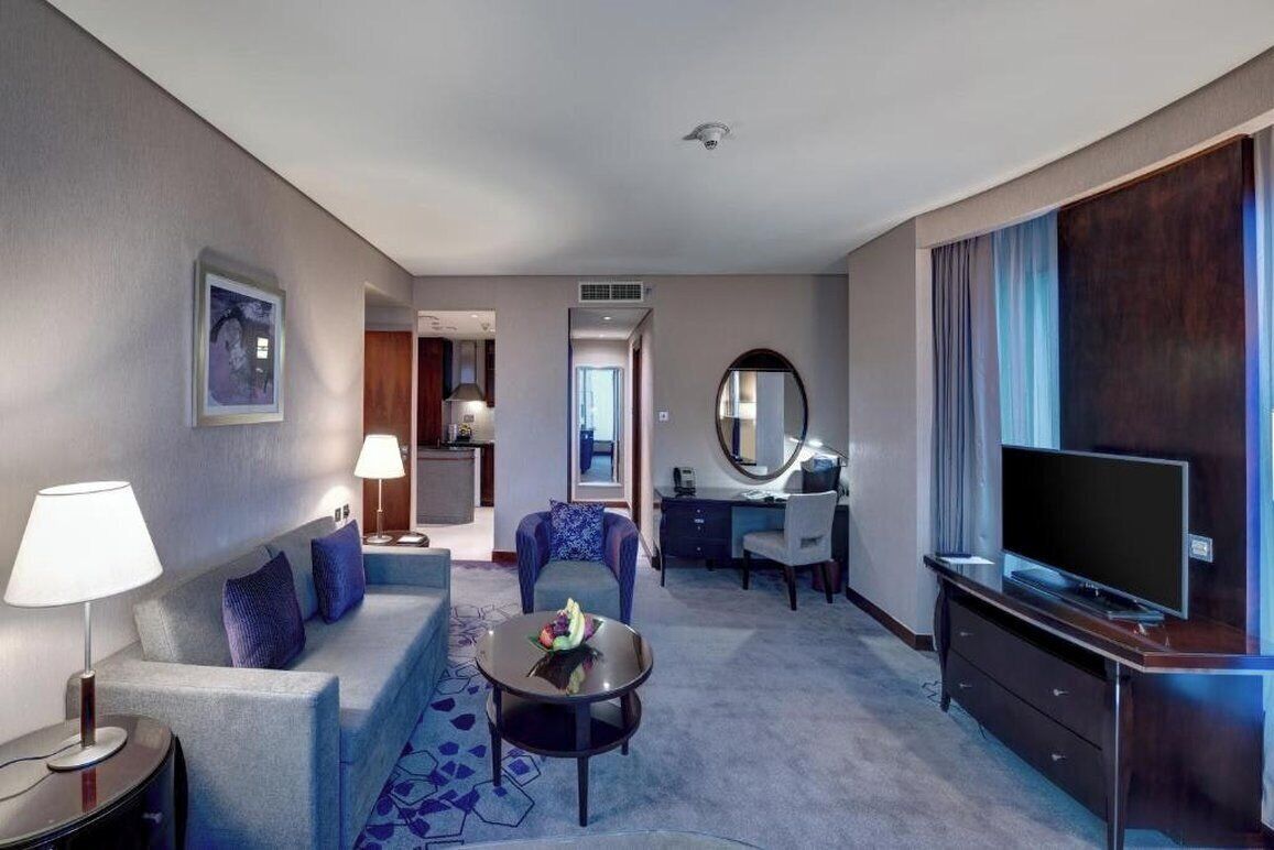 Una habitación de hotel con sofá, mesa de centro, televisión, escritorio y espejo.
