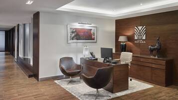 A modern reception area with a wooden desk, two leather chairs, a framed artwork, a lamp, and a statue.