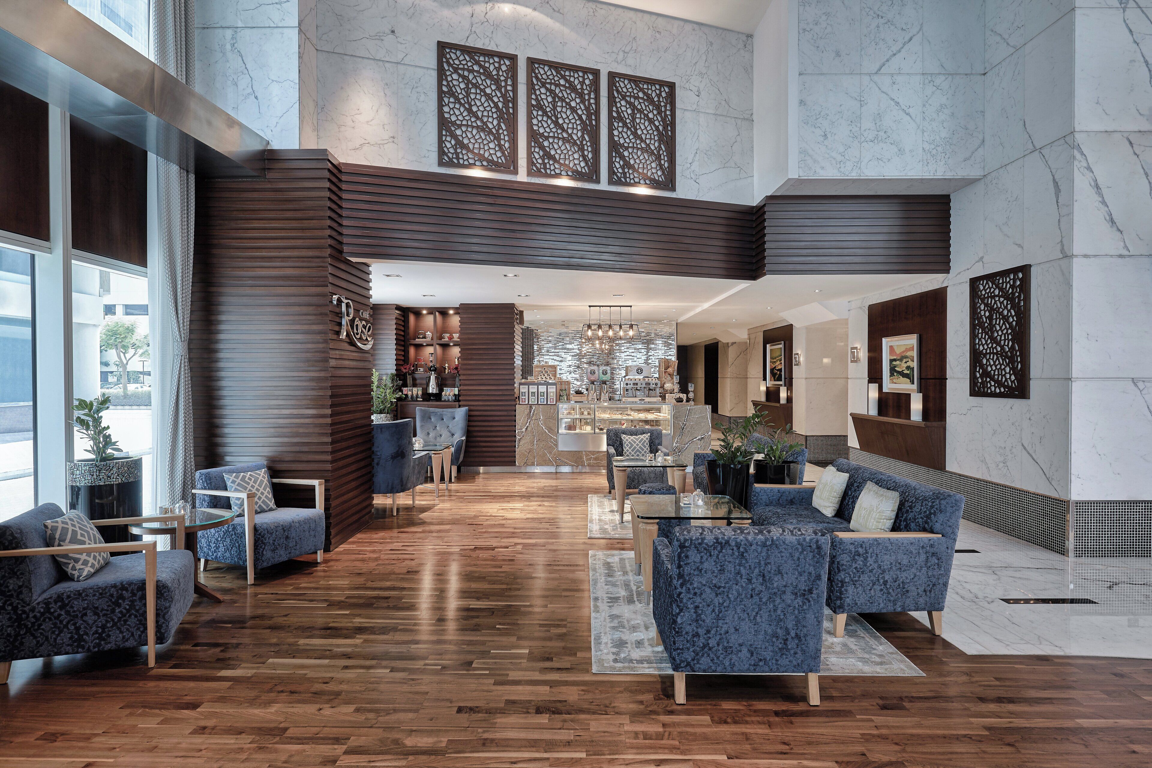 A spacious lobby with a wooden floor, blue upholstered seating, and a reception desk.