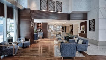A spacious lobby with a wooden floor, blue upholstered seating, and a reception desk.