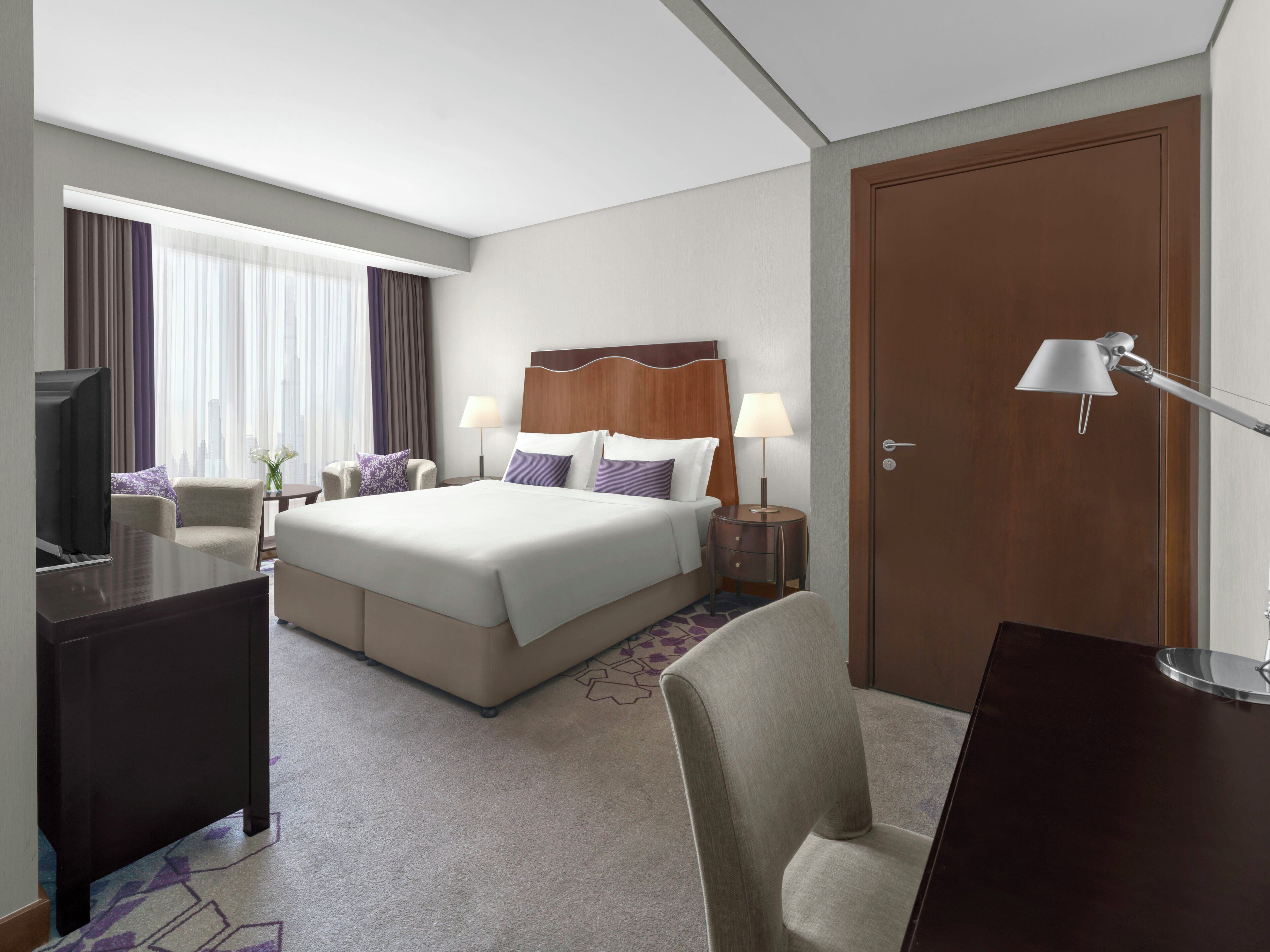Een hotelkamer met een bed, een bureau, een stoel, een televisie, een lamp en een deur.