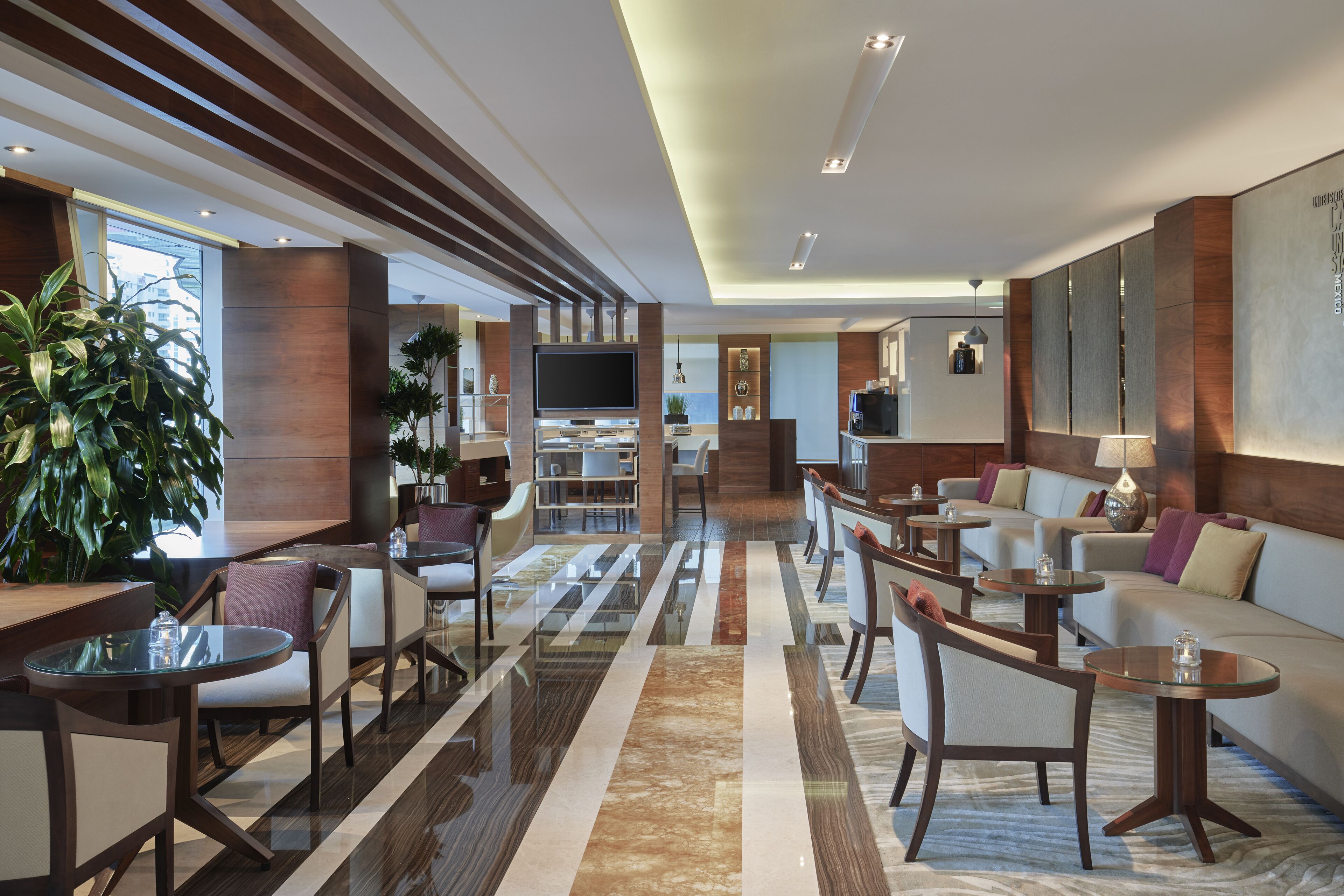 Een moderne hotellobby met een centrale zithoek, een televisie en een receptiebalie.