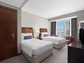 Habitación de hotel con dos camas, un escritorio, una silla y un televisor.