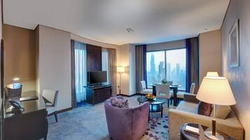 Quarto de hotel com escrivaninha, uma cadeira roxa, sofá, mesa de jantar e televisão.