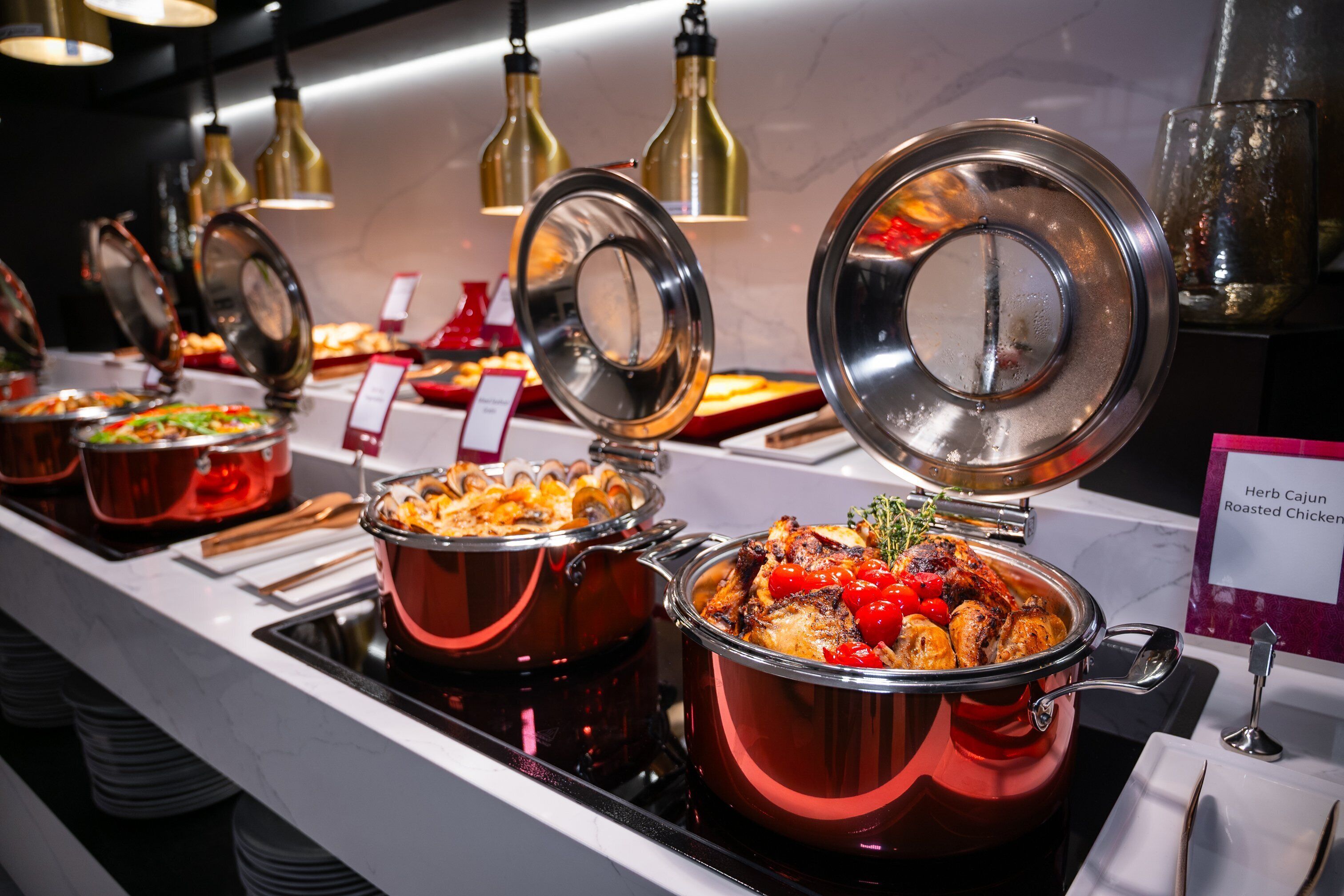 A buffet with various dishes, including a pot of roasted chicken and a dish labeled "Herb Cajun Roasted Chicken".