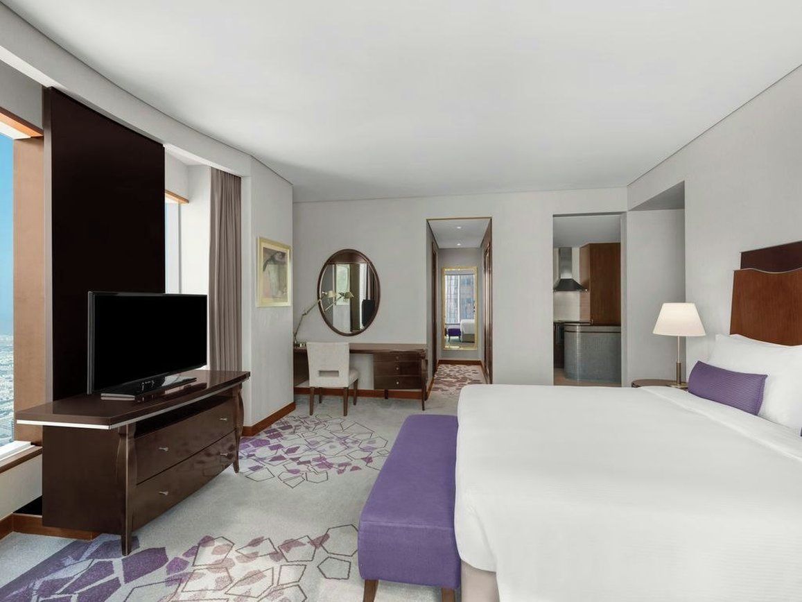 A hotel room with a bed, a desk, a television, a mirror, and a bathroom visible through an open door.