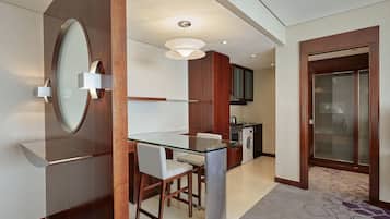 Une chambre d’hôtel moderne dotée d’une table à manger en verre, d’une cuisine intégrée et d’un espace salle de bain séparé.