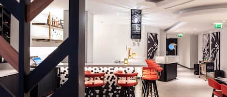 A modern bar area with a central island, red bar stools, and a hexagonal patterned floor.