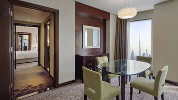 Ein Hotelzimmer mit Glastisch, vier Stühlen, einem Bett, einem Spiegel und Blick auf eine Stadtlandschaft.