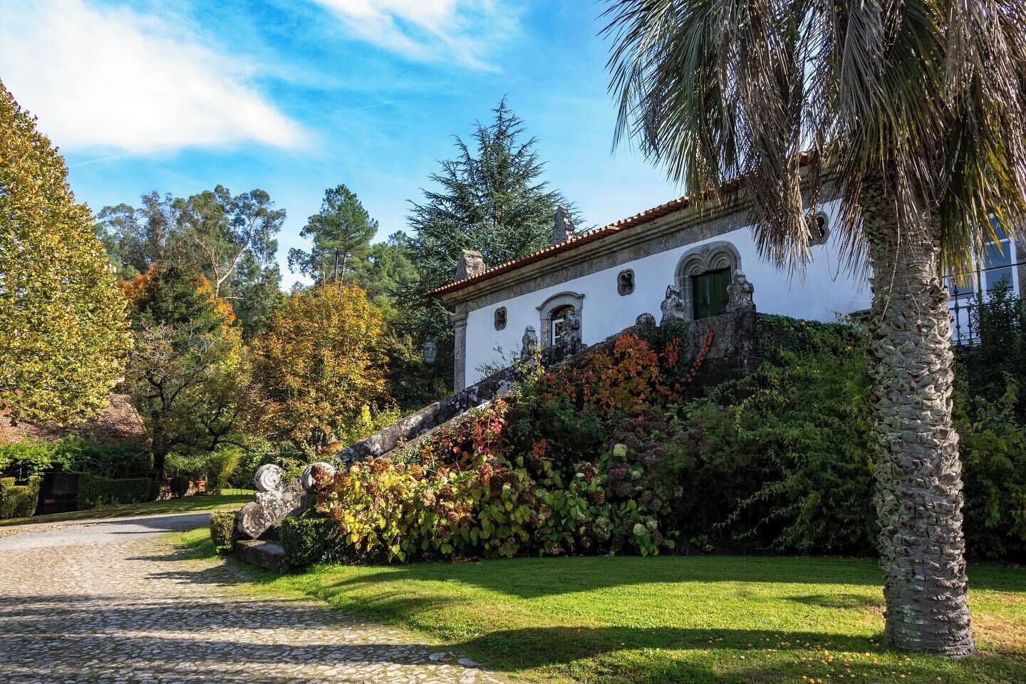 A white building with a red-tiled roof, surrounded by lush greenery and trees.