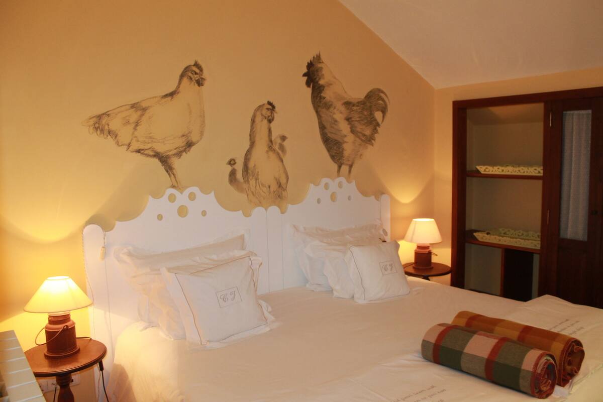 A bedroom with a bed, two bedside lamps, and a wall mural of chickens.