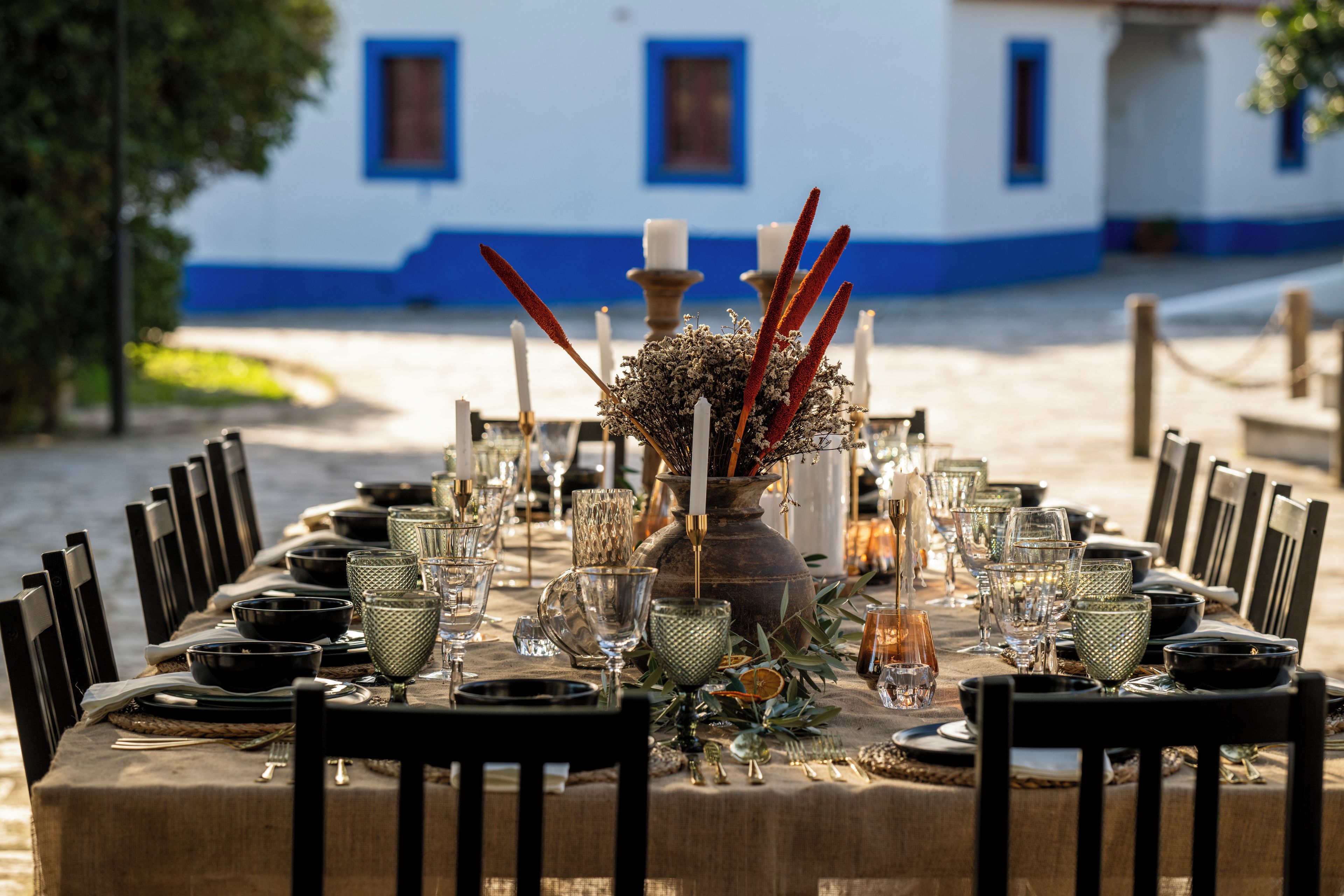 Una mesa dispuesta para una comida, con sillas, un florero con flores secas y velas.