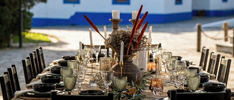 Una mesa dispuesta para una comida, con sillas, un florero con flores secas y velas.