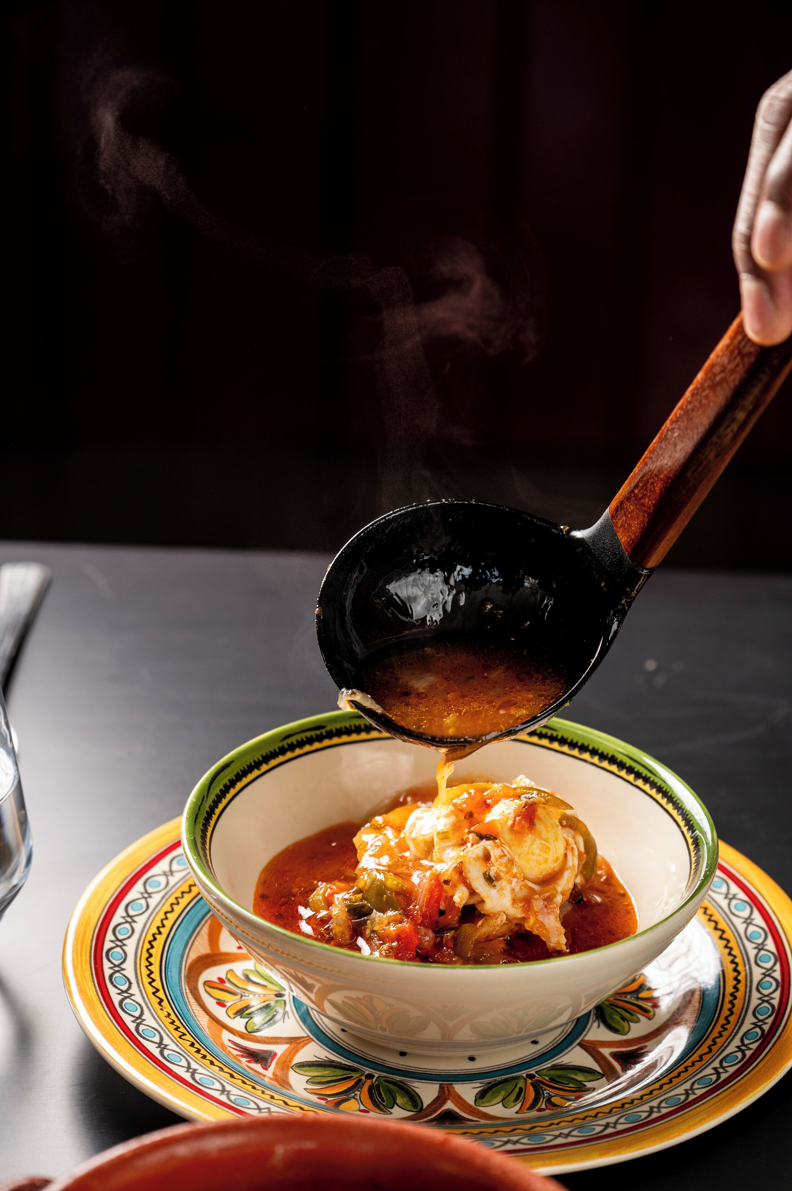 Uma tigela de sopa com vapor subindo, colocada sobre um prato colorido.