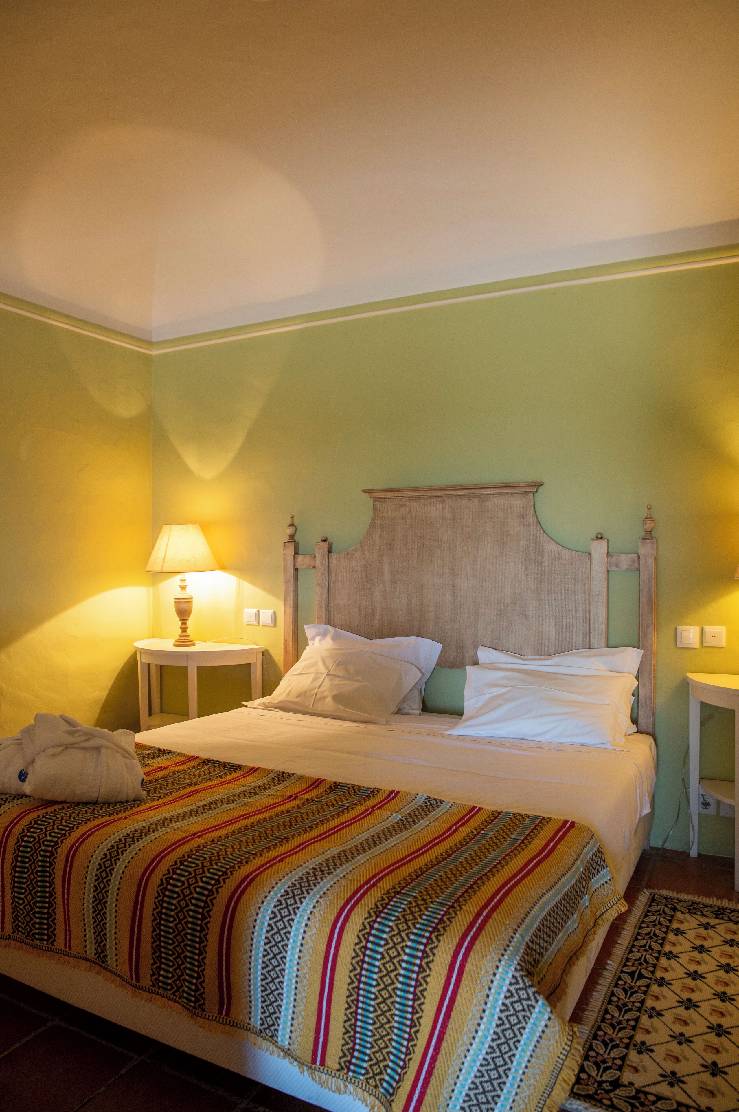 A bed with a wooden headboard, a colorful striped blanket, and a bedside lamp.
