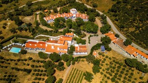 An aerial view of a resort with multiple buildings, a swimming pool, and surrounding greenery.