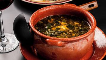 Un tazón de sopa con tapa, una copa de vino tinto y un plato con rebanadas de pan.