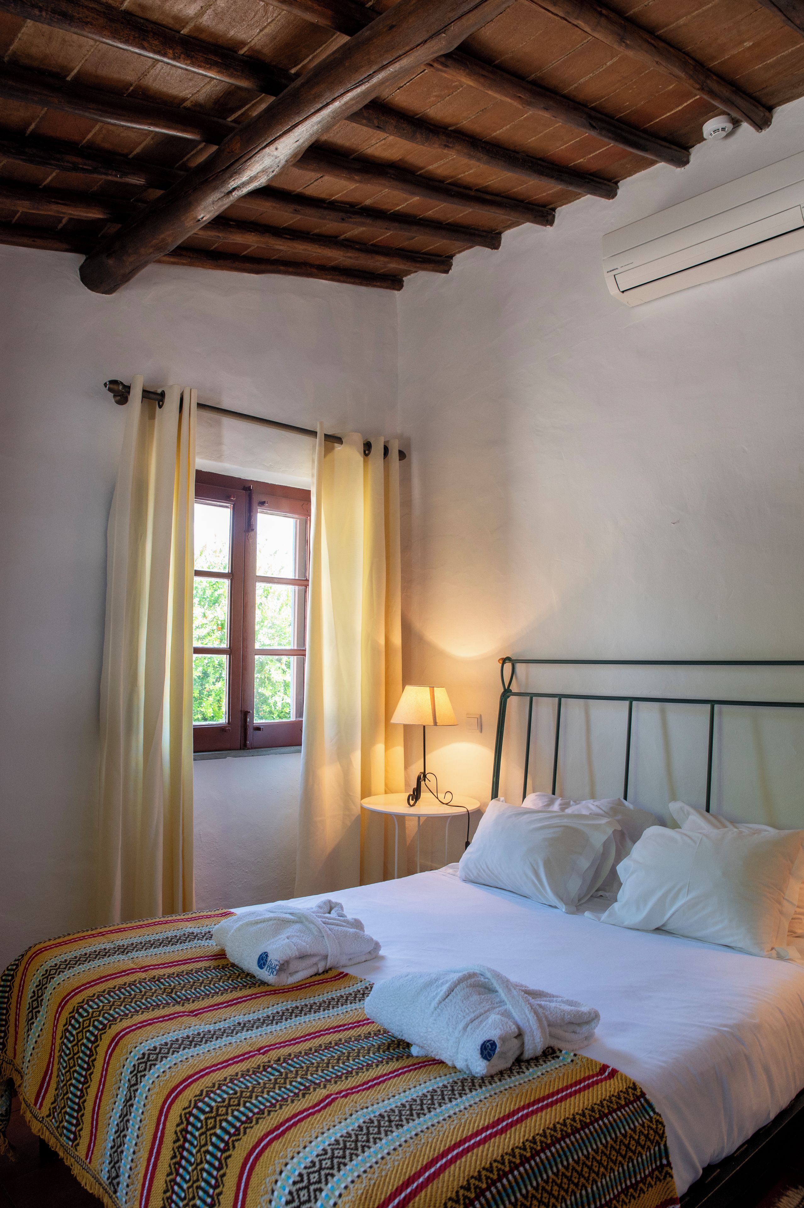 Een slaapkamer met een bed, een raam met gordijnen, een bedlamp en een geborduurde deken.