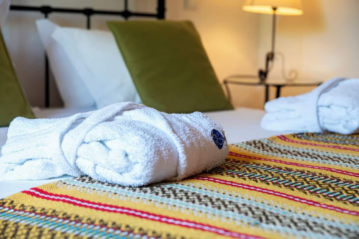 Una cama bien hecha con un edredón de colores, una almohada verde y una toalla blanca.