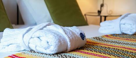 A neatly made bed with a colorful blanket, a green pillow, and a white towel.