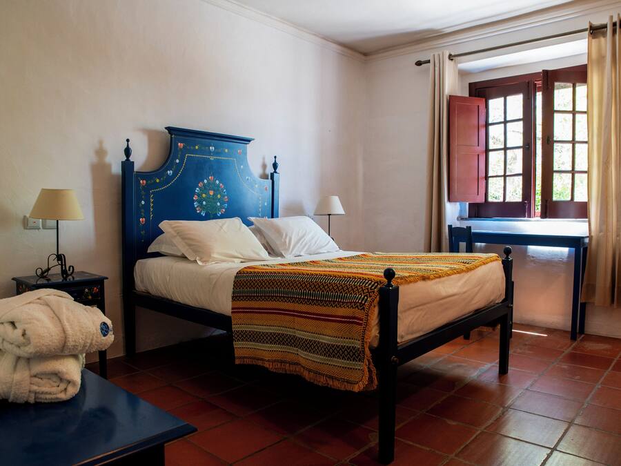 A room with a bed, a nightstand, a table, and a window with curtains.