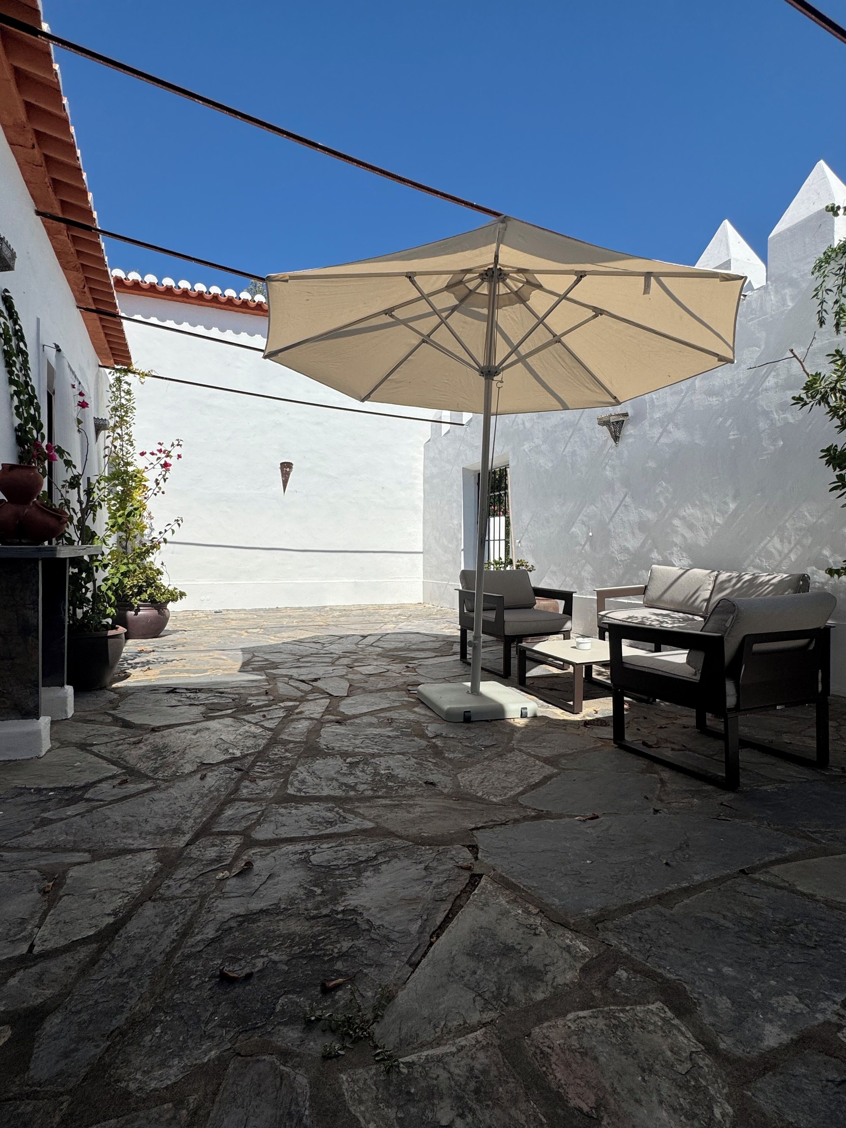 Une terrasse avec un sol en pierre, du mobilier d’extérieur et un grand parasol.