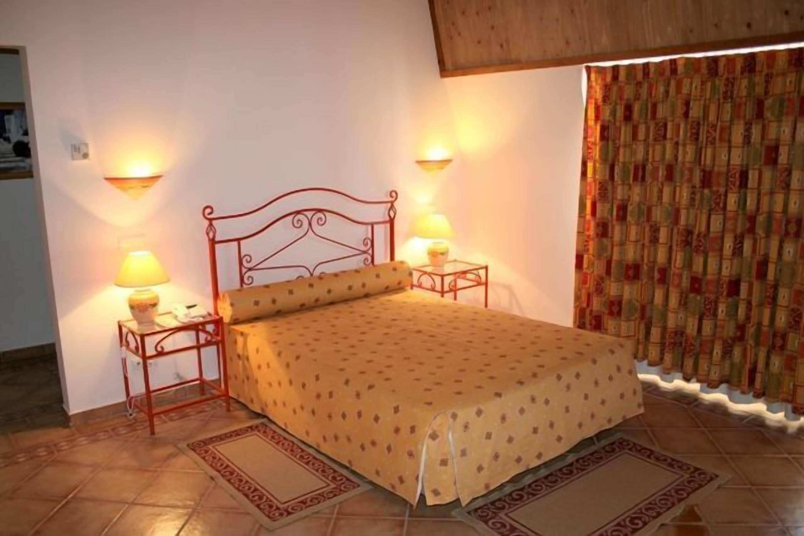 A single bed with a headboard, two bedside tables with lamps, patterned bedding, and a patterned rug.
