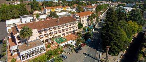 Vista aérea de un pueblo costero con un hotel destacado que cuenta con un patio central, varios balcones y un estacionamiento.
