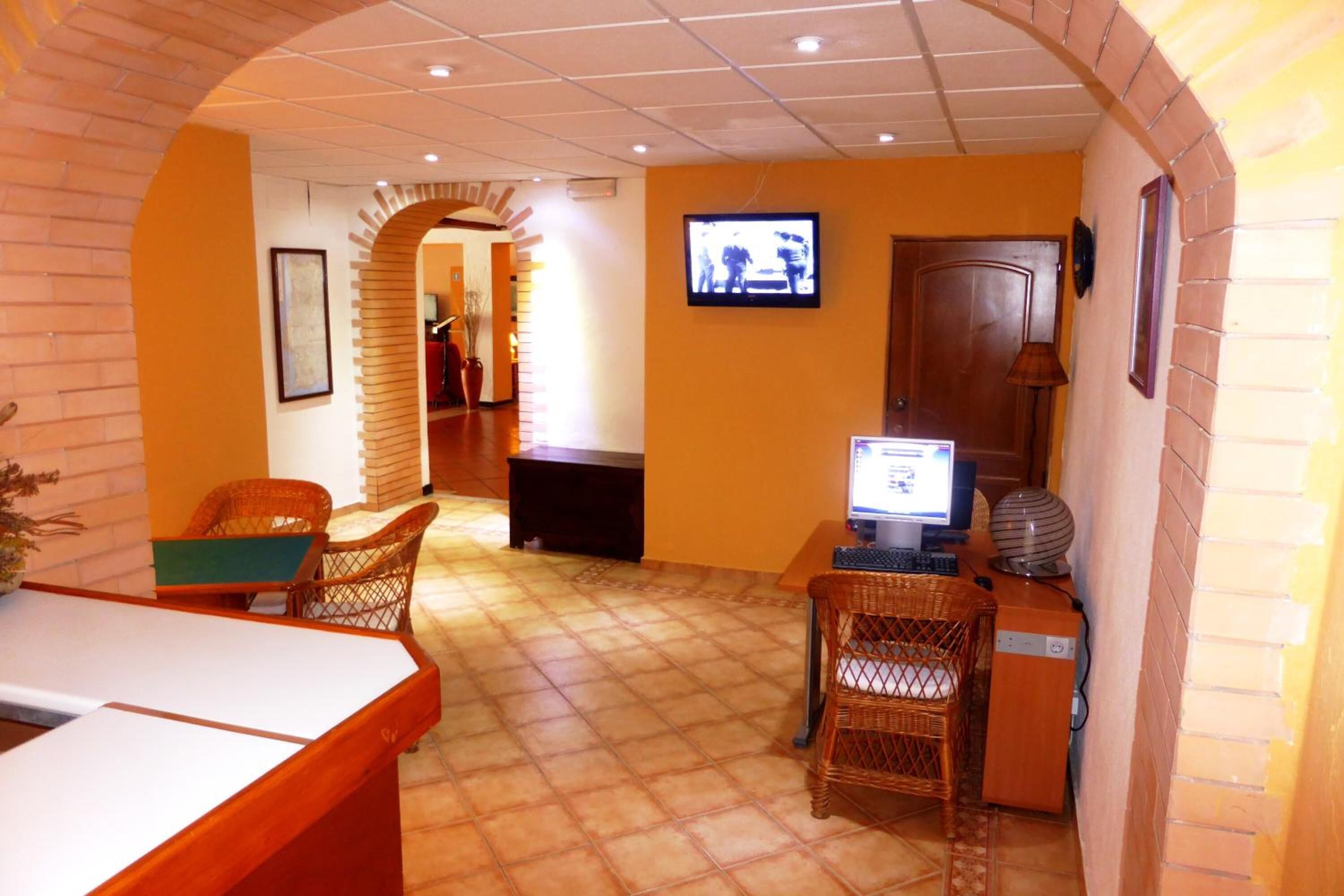 Un área de recepción con suelo de baldosas, mobiliario de mimbre, una computadora y un televisor.