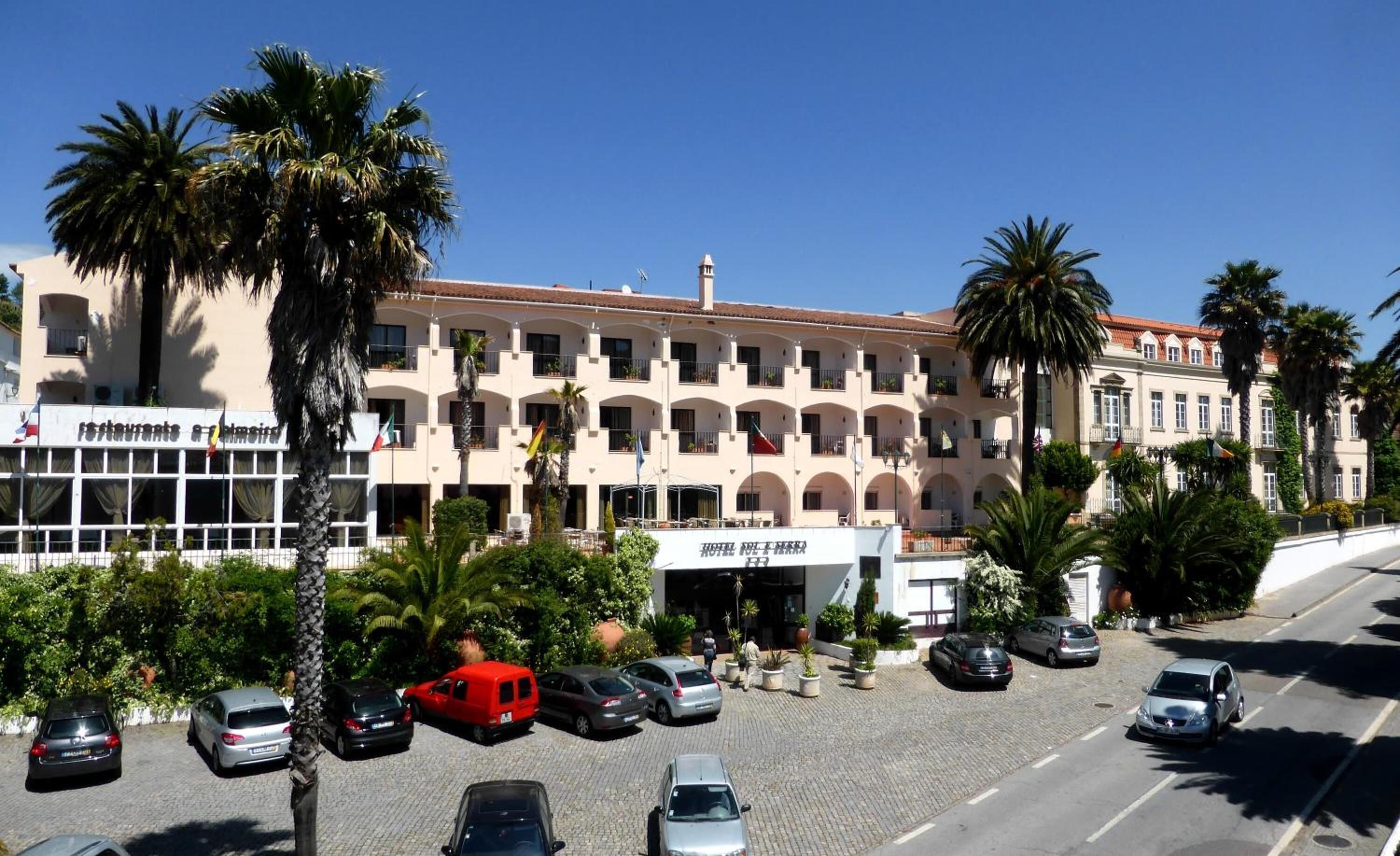 A hotel with a central courtyard, multiple balconies, and a parking area with several cars.