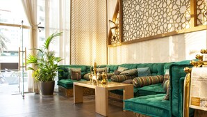 A green sofa set with a wooden coffee table, a potted plant, and a decorative wall with geometric patterns. - Samaya Hotel Deira (Dubai)