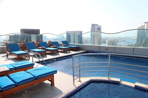 A rooftop pool area with blue-striped lounge chairs and a view of the cityscape.